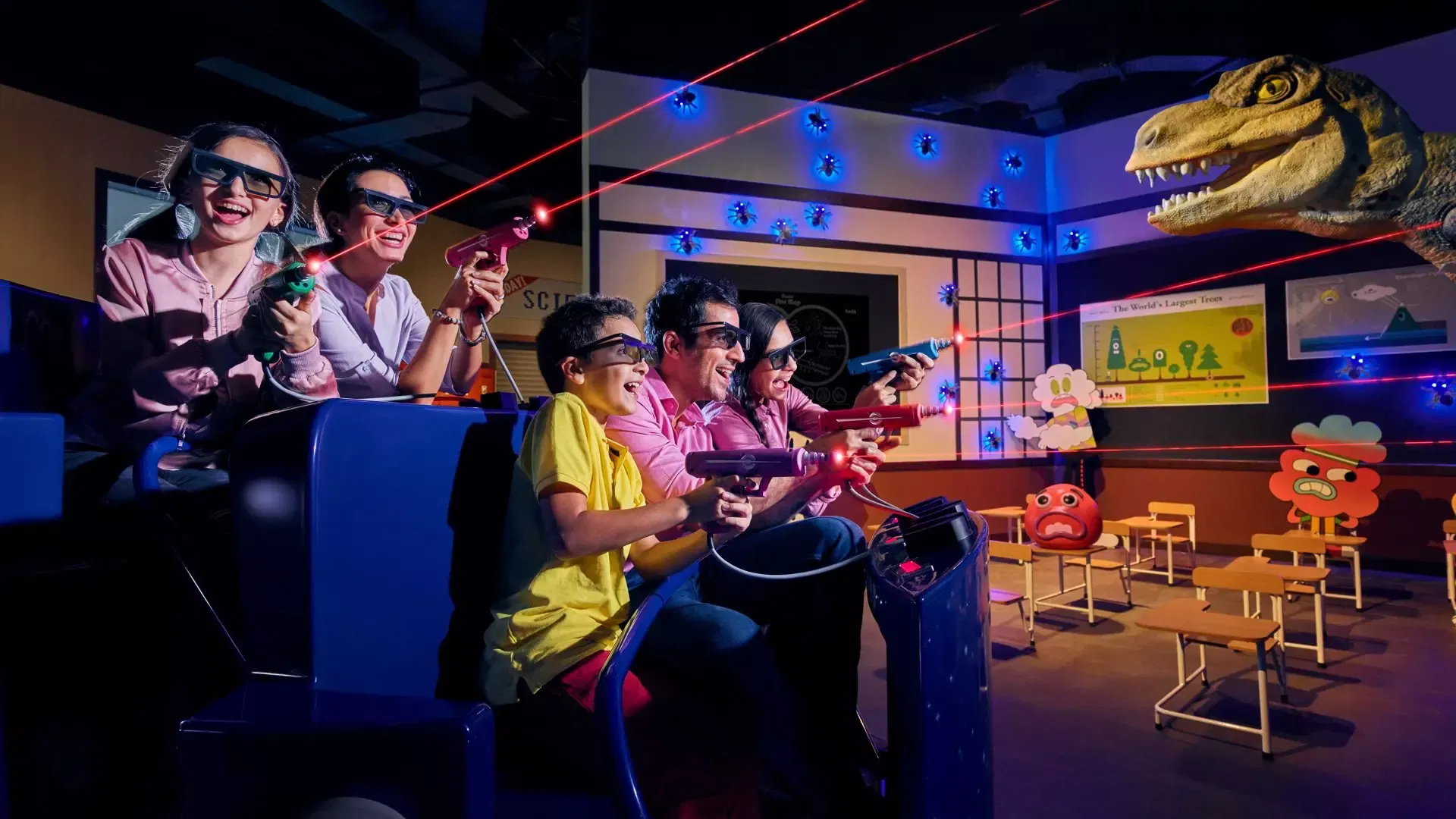 A family wearing 3D glasses aims laser guns at targets on the wall while sitting in a ride vehicle at IMG Worlds of Adventure Theme Park.