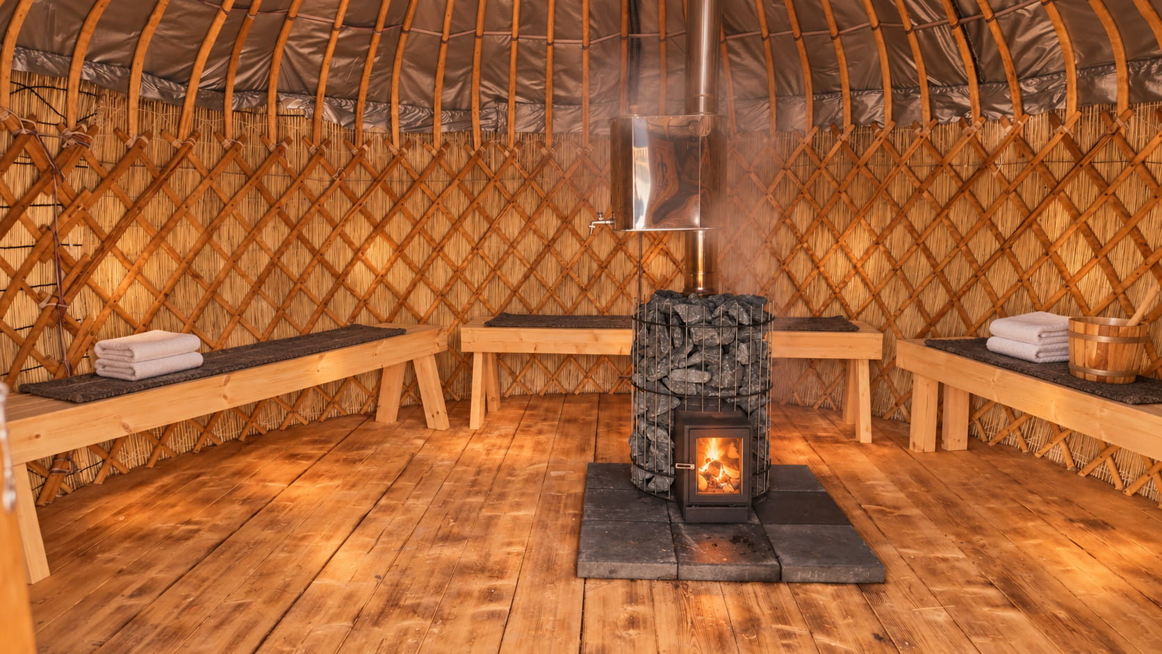 Interior of a handcrafted wooden yurt sauna with curved benches surrounding a central wood-burning stone stove.