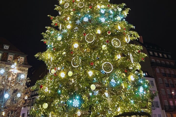 Vue rapprochée du sommet du Grand Sapin de Noël illuminé de Strasbourg, décoré de boules, de lumières blanches, jaunes et bleues.