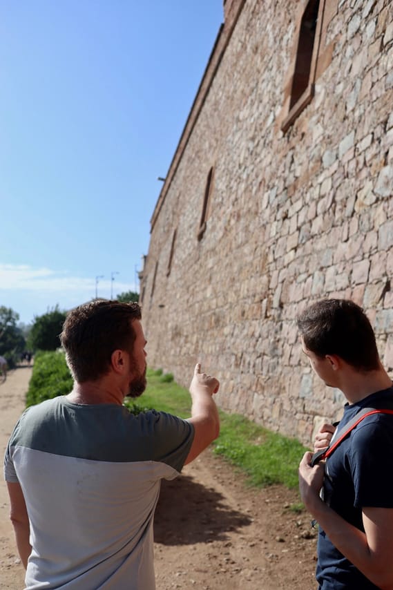 The tour guide is standing with his guest in front of a massive stone wall, one side of Montjuic Castle.