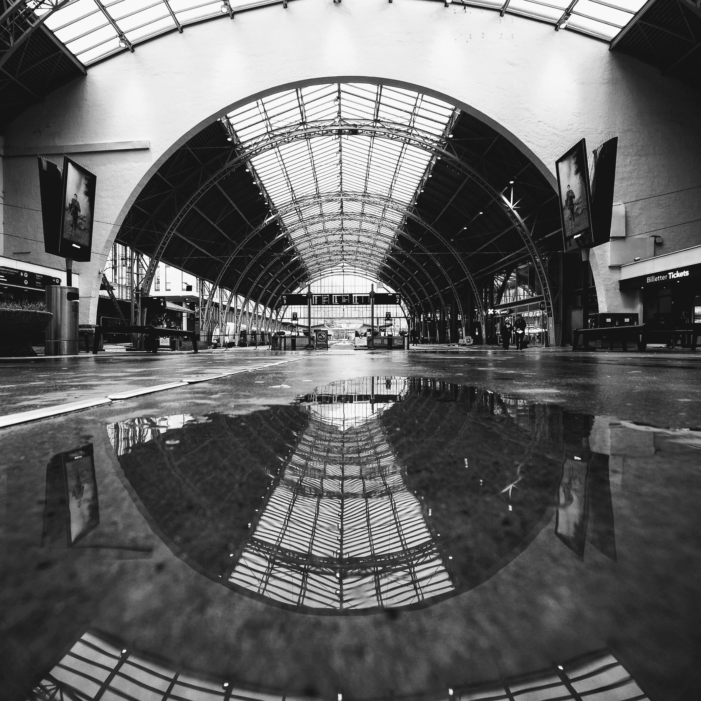 Black-and-white image of the trainsation hall reflected on wet ground, showing creative composition explored during the photowalk.
