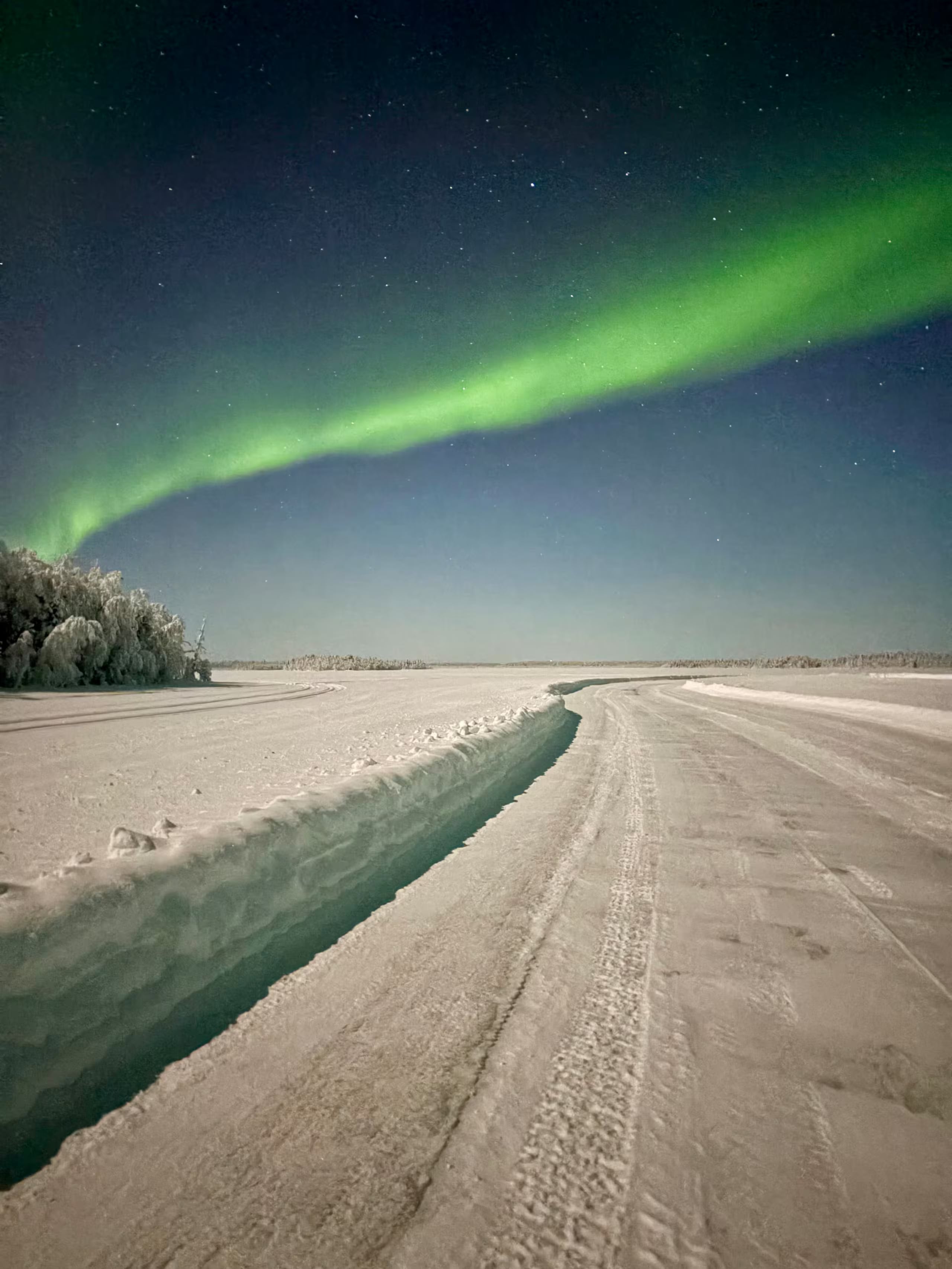Green Northern Lights above a snowy route on frozen Rautusjärvi lake near Levi