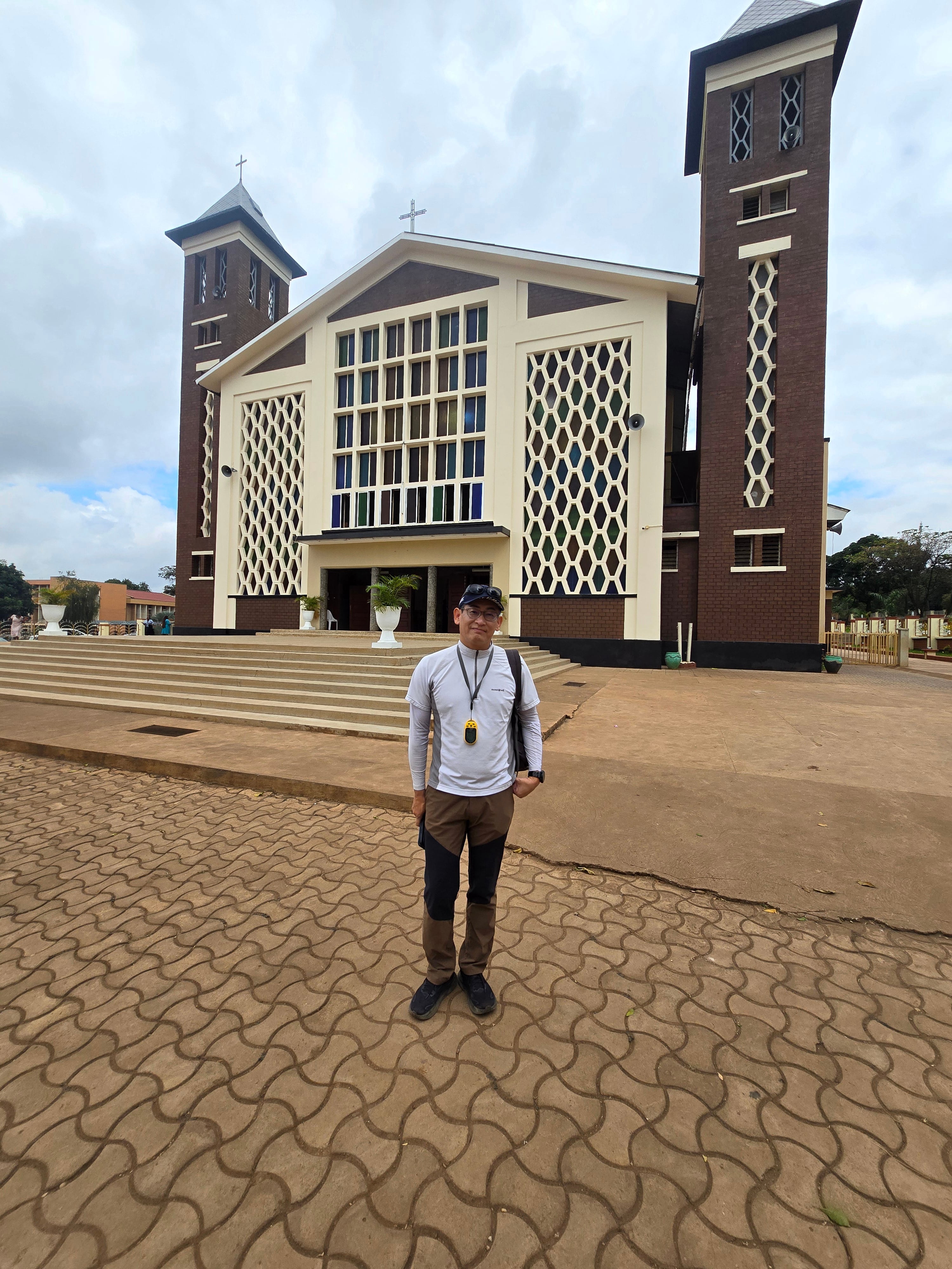 A guide standing in the outdoor paved grounds outside Christ the King Cathedral building in Moshi.