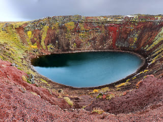 Red lava rock and green moss decorating the rim of Kerid volcanic crater