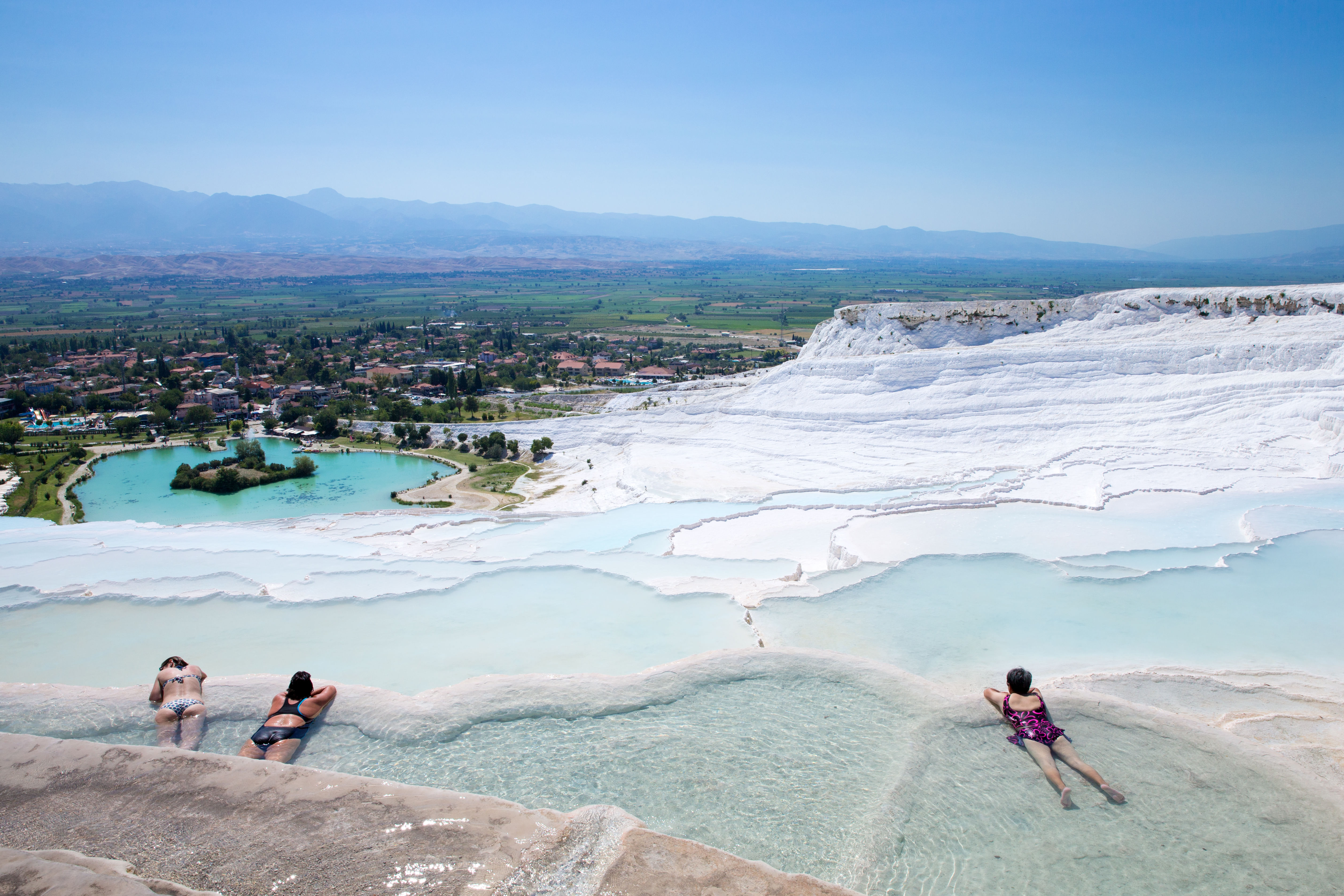 “Tourists bathing and relaxing in the warm, turquoise thermal pools on the white travertine terraces of Pamukkale.”