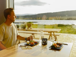 A person enjoying a great meal and the beautiful view from the restaurant at Vök baths over lake Urriðavatn.