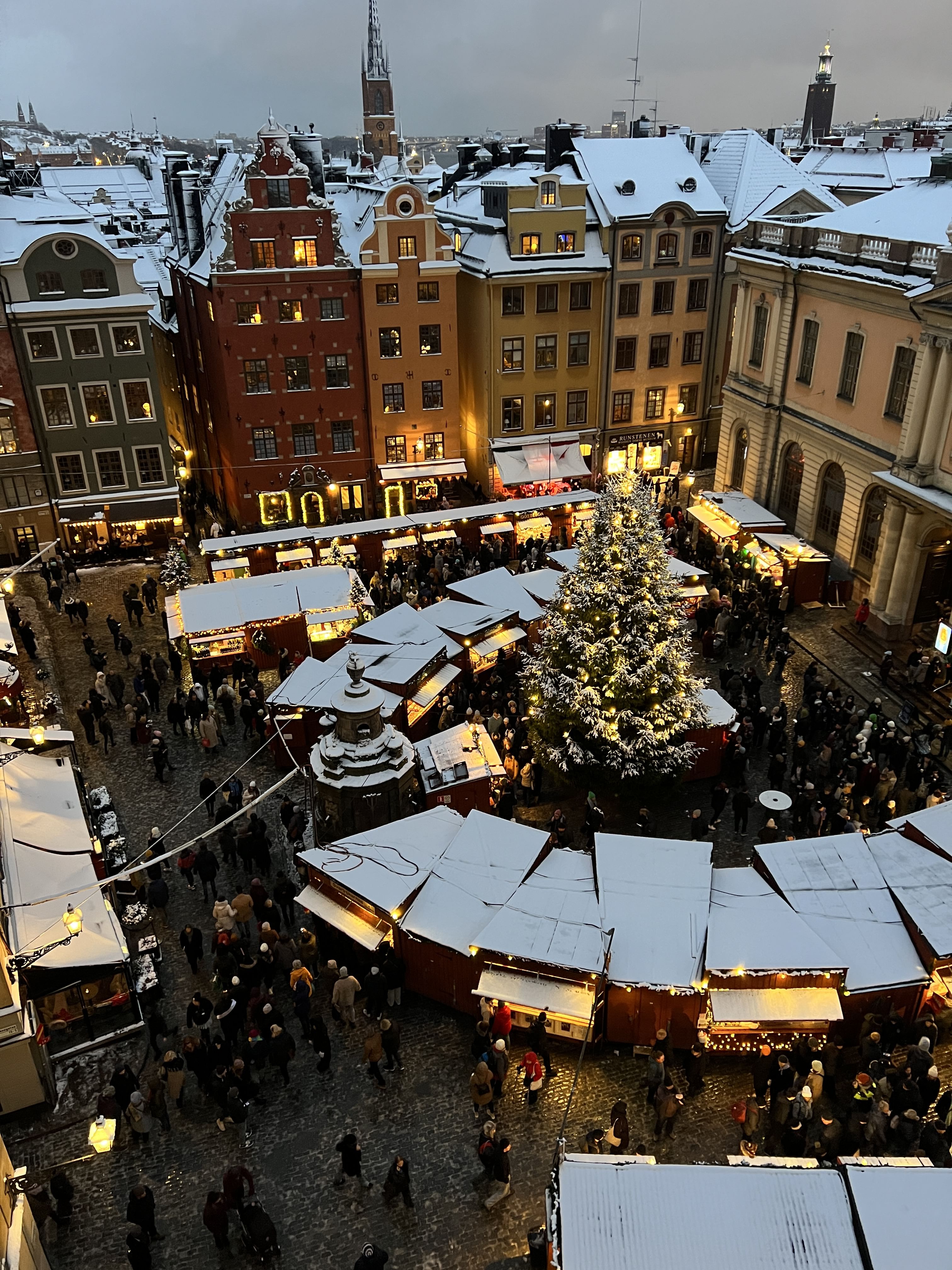 Aerial view of Stortorget in Stockholm’s Old Town during winter, with snow-covered roofs, a large Christmas tree, and market stalls surround