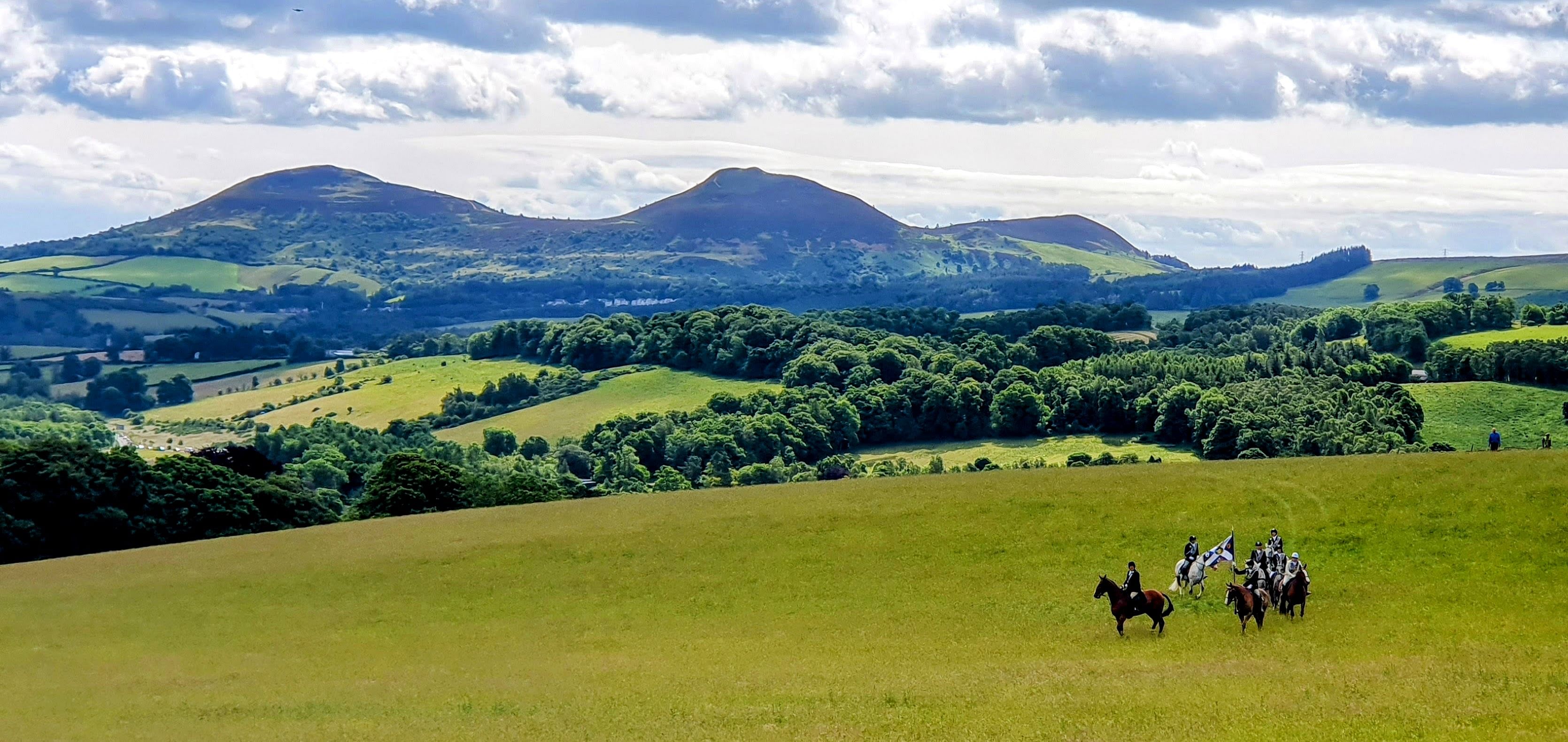 Summers day country hillside view with a gathering of mounted horses. The leader is carrying a ceremonial saltire flag.