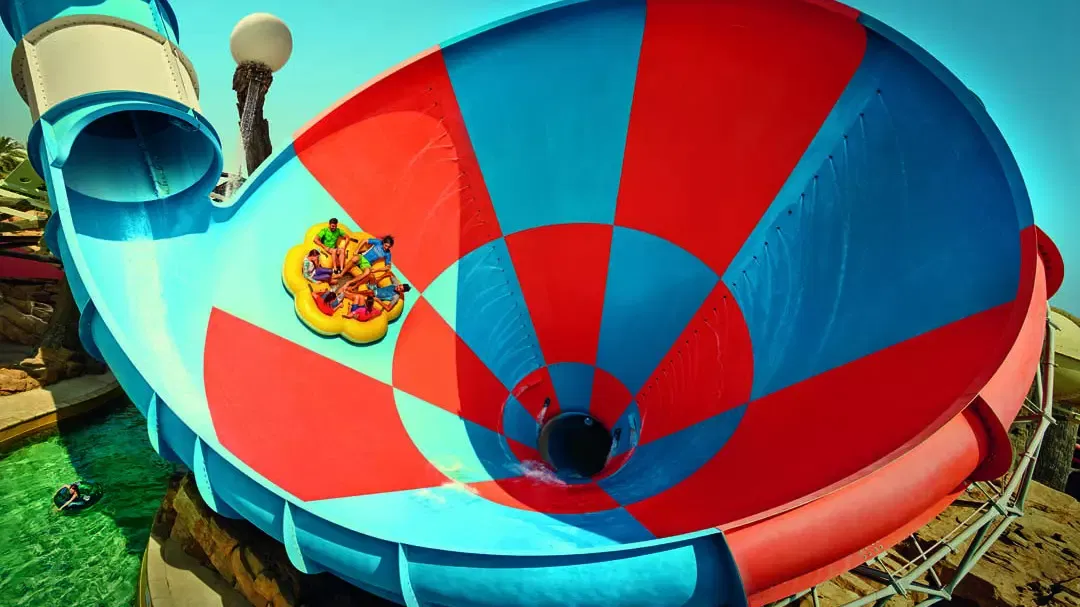 A group of people in a raft plunge down a giant red and blue funnel-shaped water slide at Yas Waterworld, Abu Dhabi.