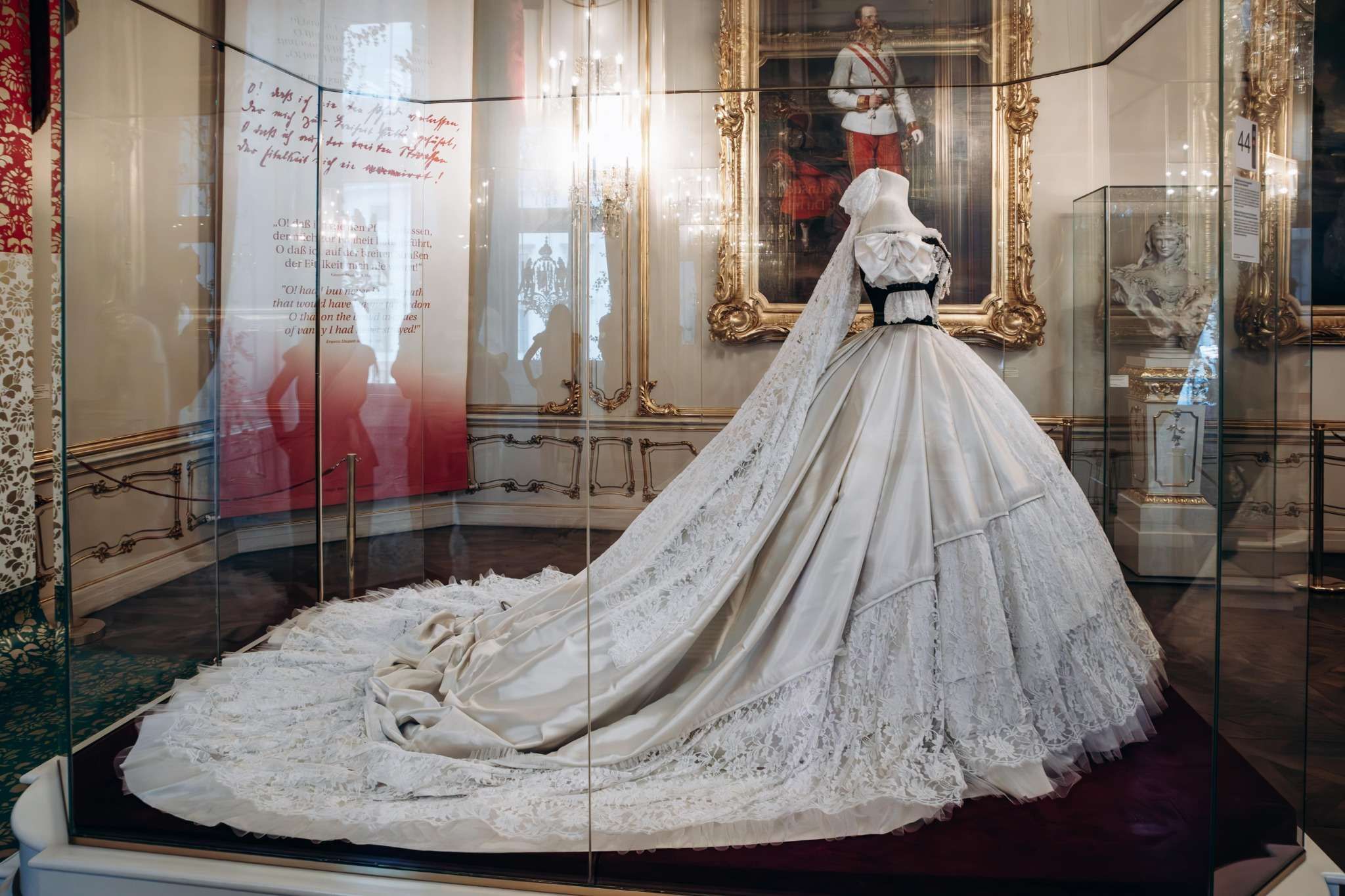 White 19th-century ball gown with long train in a glass case, displayed at the Sisi Museum