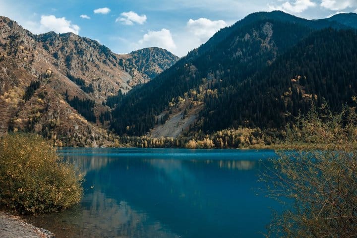 Panoramic view of Issyk Lake with turquoise water and pine-covered mountains in Kazakhstan