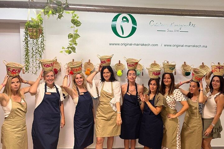 Large group of young women posing inside the workshop with their personalized embroidered baskets and hats, as a souvenir of their creative bachelorette party in Marrakech.