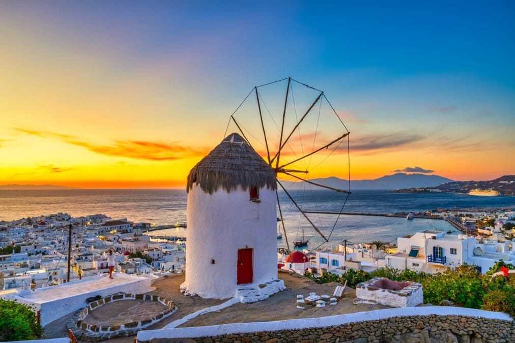 Windmühle auf Mykonos bei Sonnenuntergang mit Blick auf die Ägäis mit goldenem Licht über der Küste
