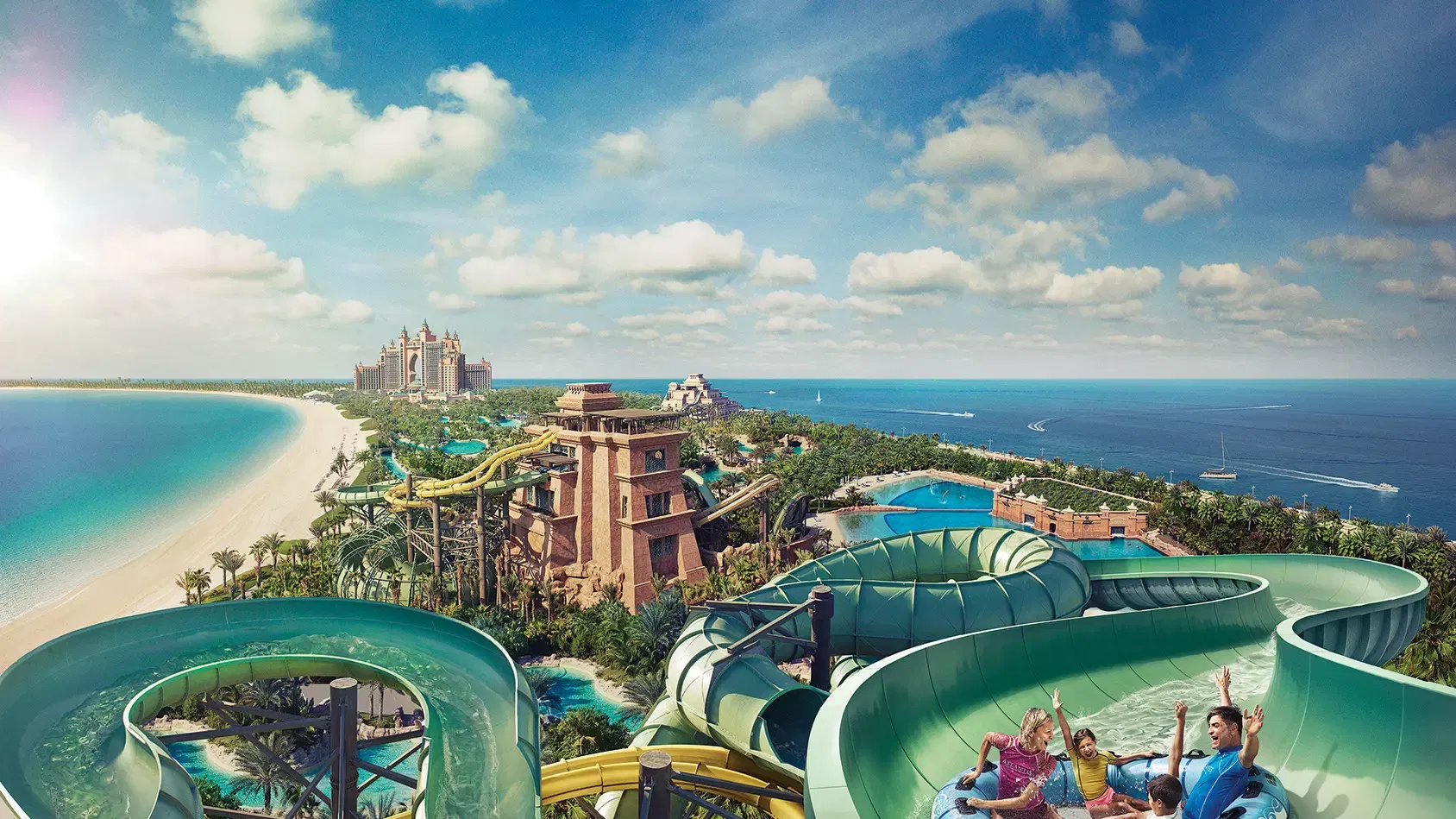 An aerial view over the twisting green and yellow slide flumes and the stone Ziggurat tower, with the Atlantis hotel, the beach and the Arabian Gulf beyond, at Aquaventure Waterpark