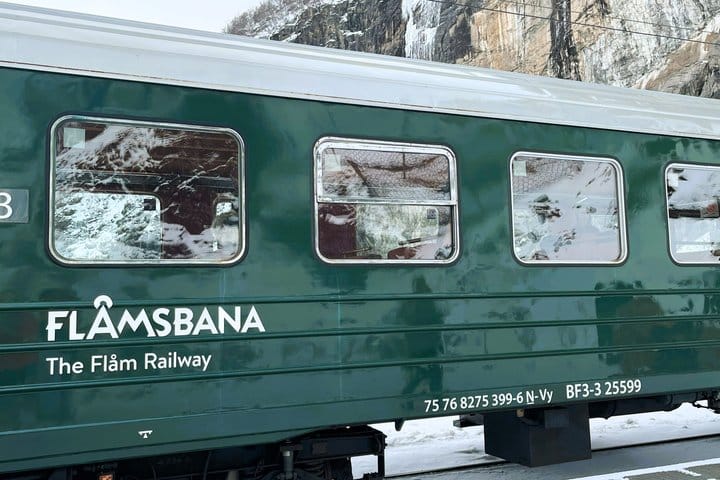 Green Flåm Railway carriage beside snow-covered mountain cliffs