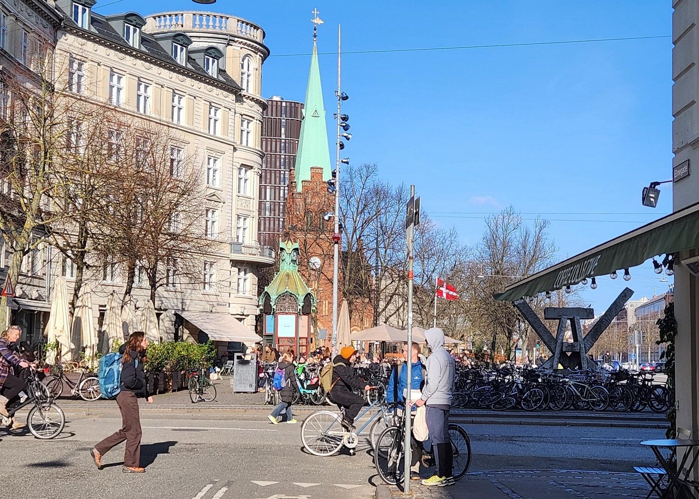 People and cyclists in a lively Nørrebro square with historic buildings and a church in Copenhagen.