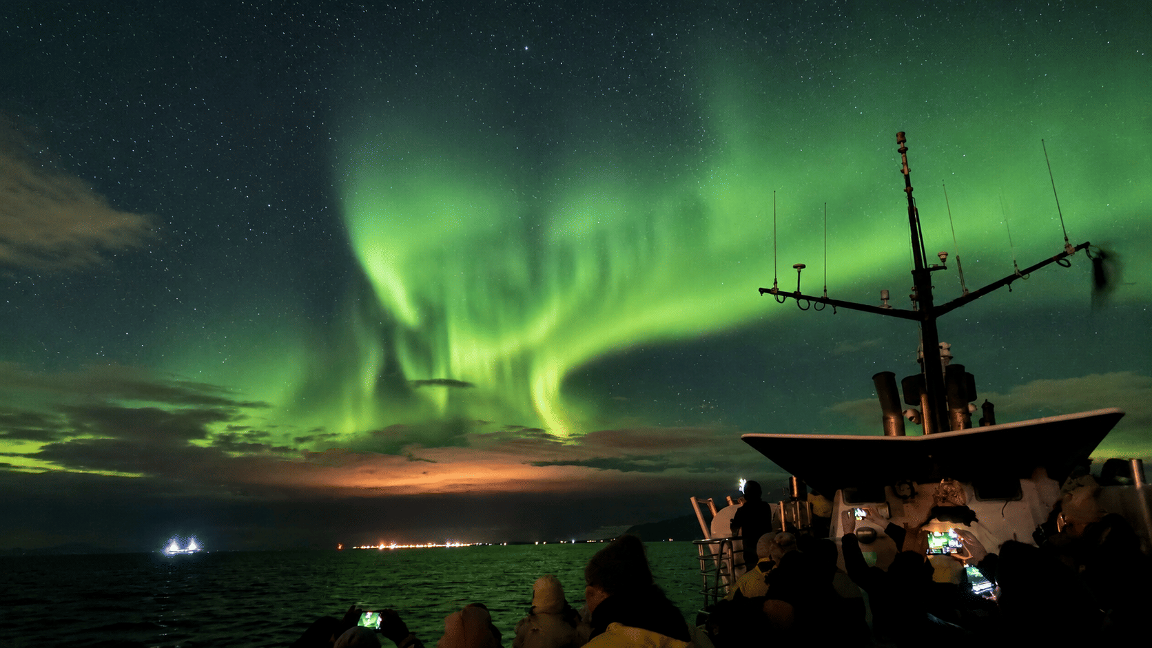 Bright green Aurora Borealis dancing above the horizon during a Northern Lights cruise in Iceland.