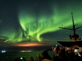 Bright green Aurora Borealis dancing above the horizon during a Northern Lights cruise in Iceland.