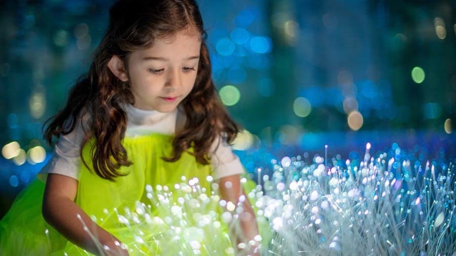 A young girl in a yellow dress reaching into a field of glowing white fibre-optic stems at AYA Universe Dubai
