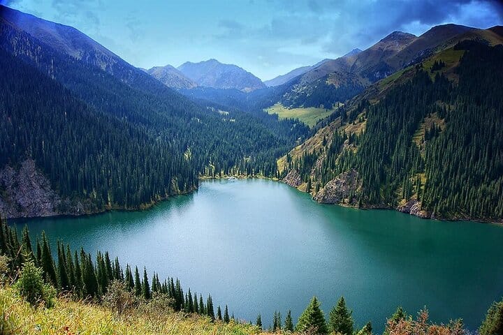 Scenic alpine lake surrounded by dense forests and steep green mountains.