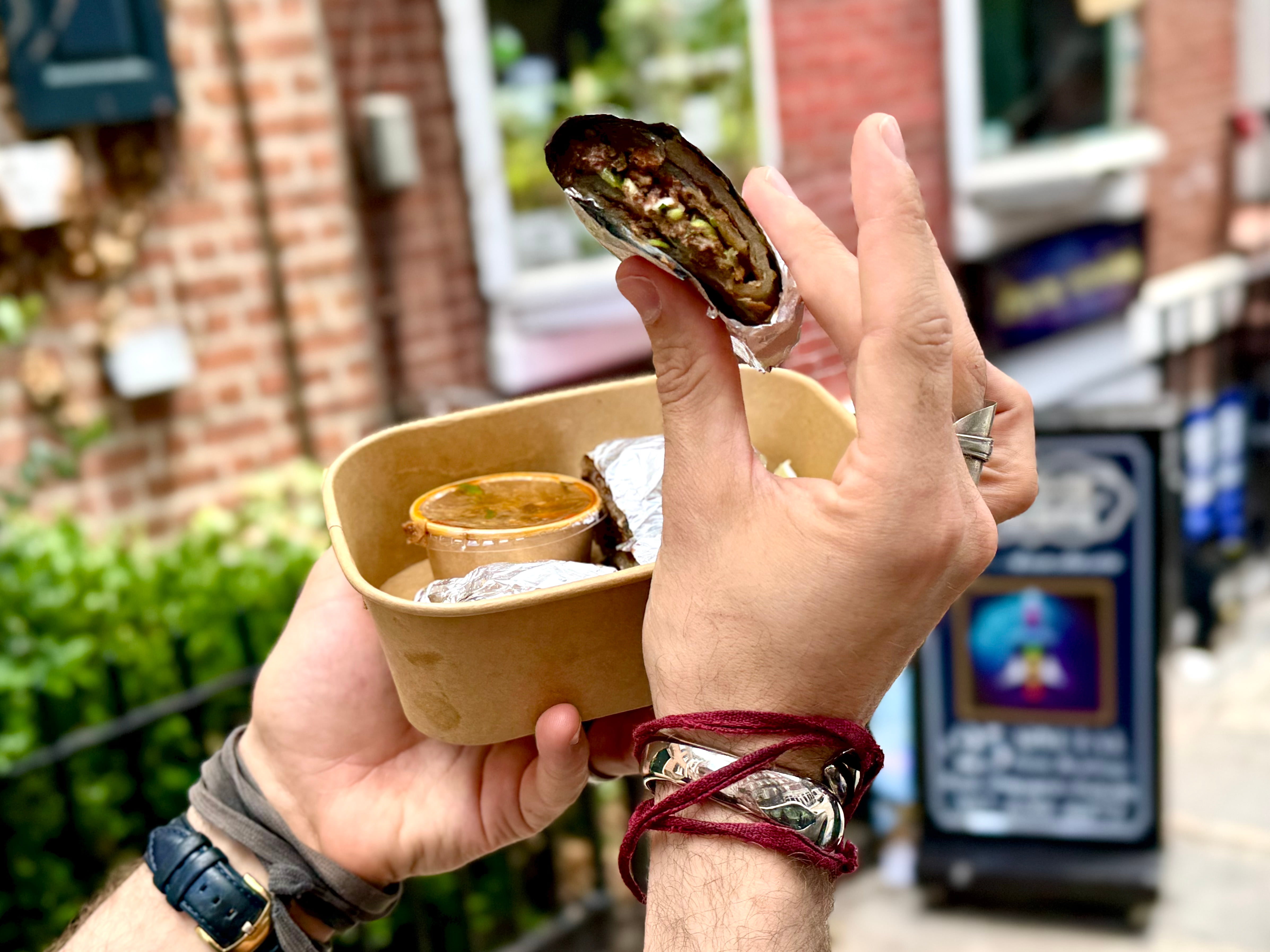 A hand holds a cut scallion pancake roll in front of a Chinese restaurant.