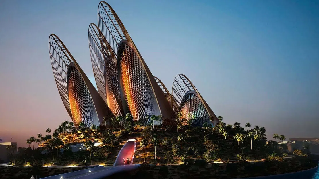 A grand building with towering, ribbed wing-like structures sits atop a landscaped hill at Zayed National Museum, Abu Dhabi.