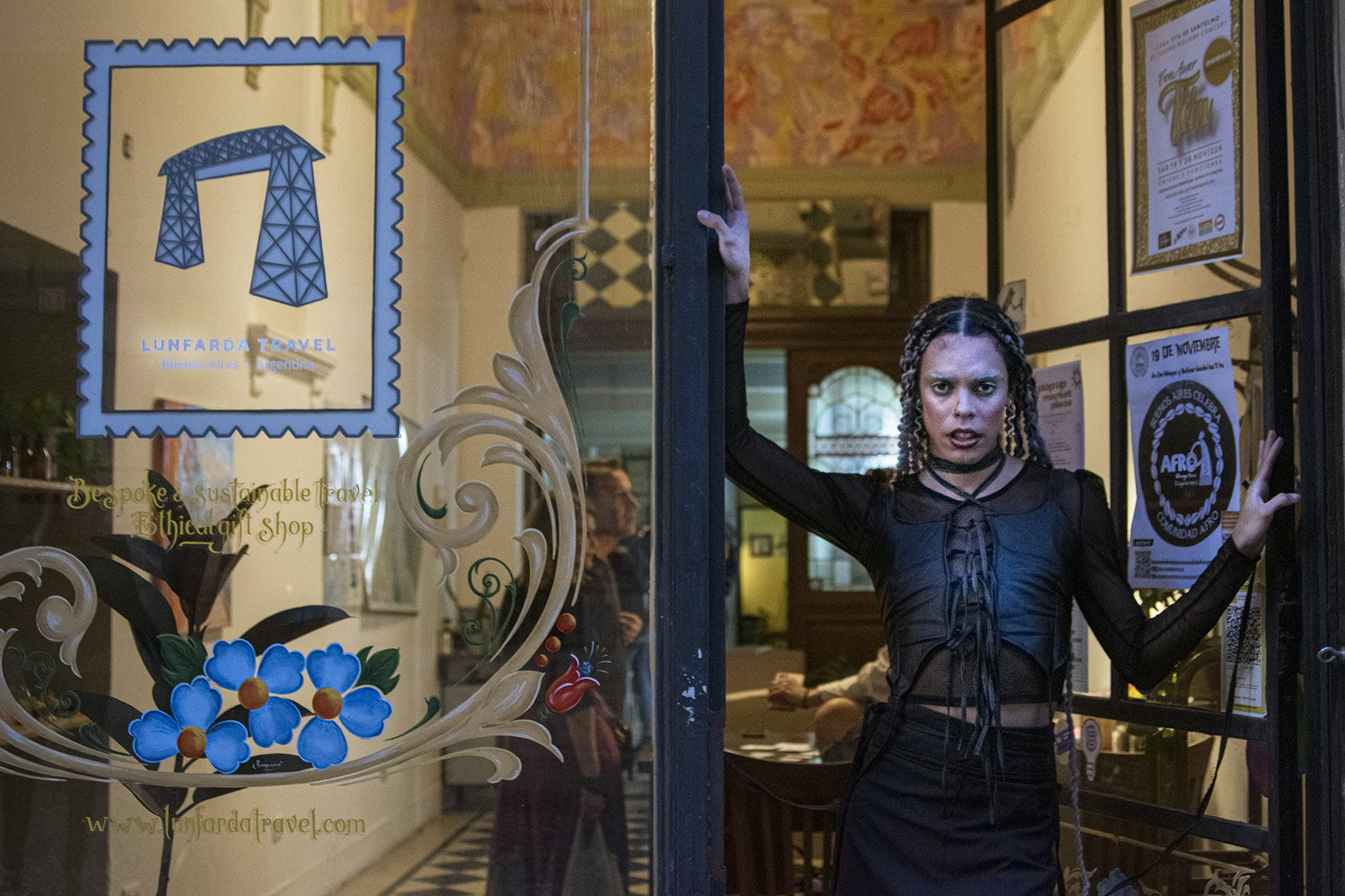 Foto of a Dragqueen standing in the door of lunfarda office with the logo at the window next to him
