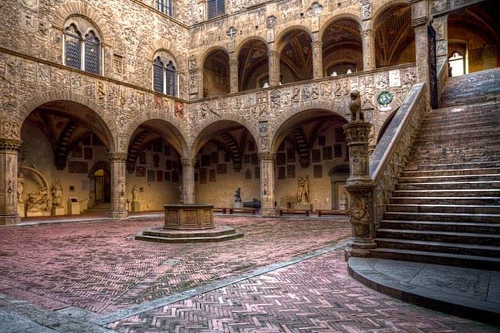 View of the internal cloister of the Bargello museum wit its decorated walls, stone staircase and stone well.