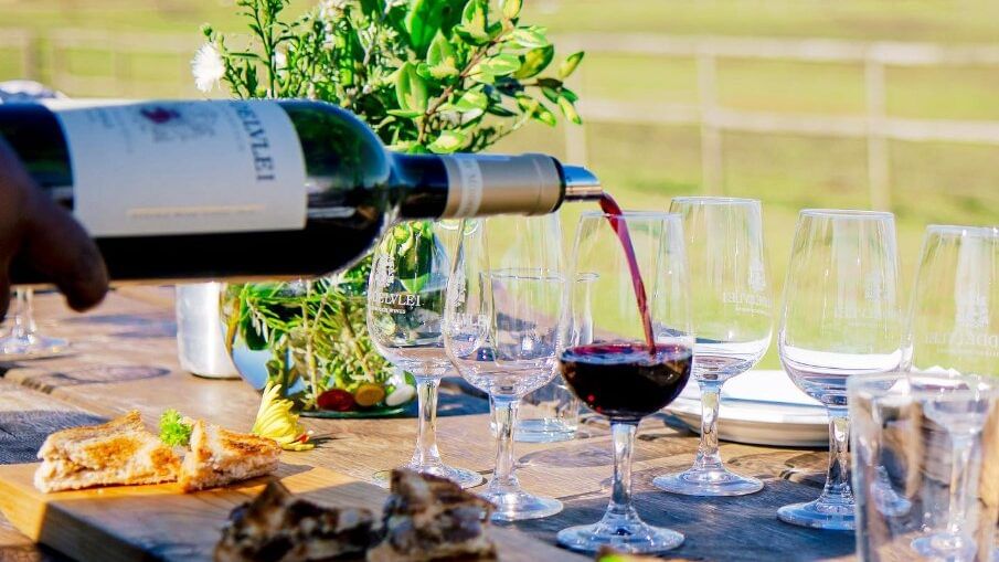 Outdoor lunch setting at Middelvlei Wine Estate with estate wine bottles and South African braai dishes in the Cape Winelands.