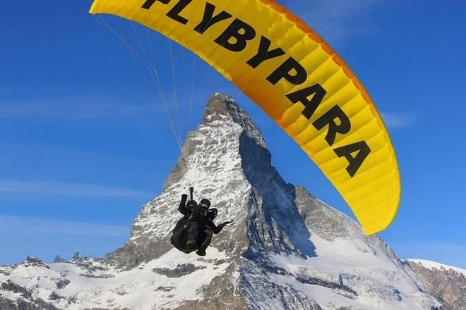 Pilot and passenger tandem paragliding above the Matterhorn in Zermatt, Switzerland with FLYBYPARA. Scenic alpine flight with panoramic moun
