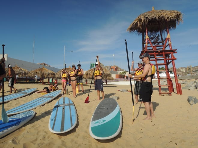 Group receiving stand up paddle board lesson on the beach in Cabo San Lucas with boards and paddles