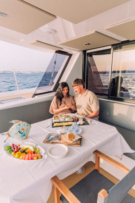 A close-up of a proposal taking place at a set dining table on a yacht, featuring an open ring box and glasses of champagne.