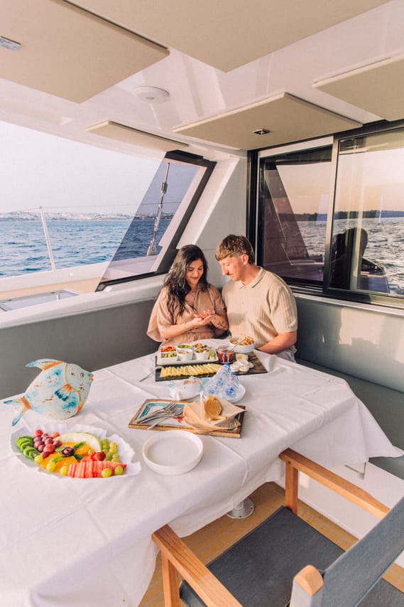 A close-up of a proposal taking place at a set dining table on a yacht, featuring an open ring box and glasses of champagne.