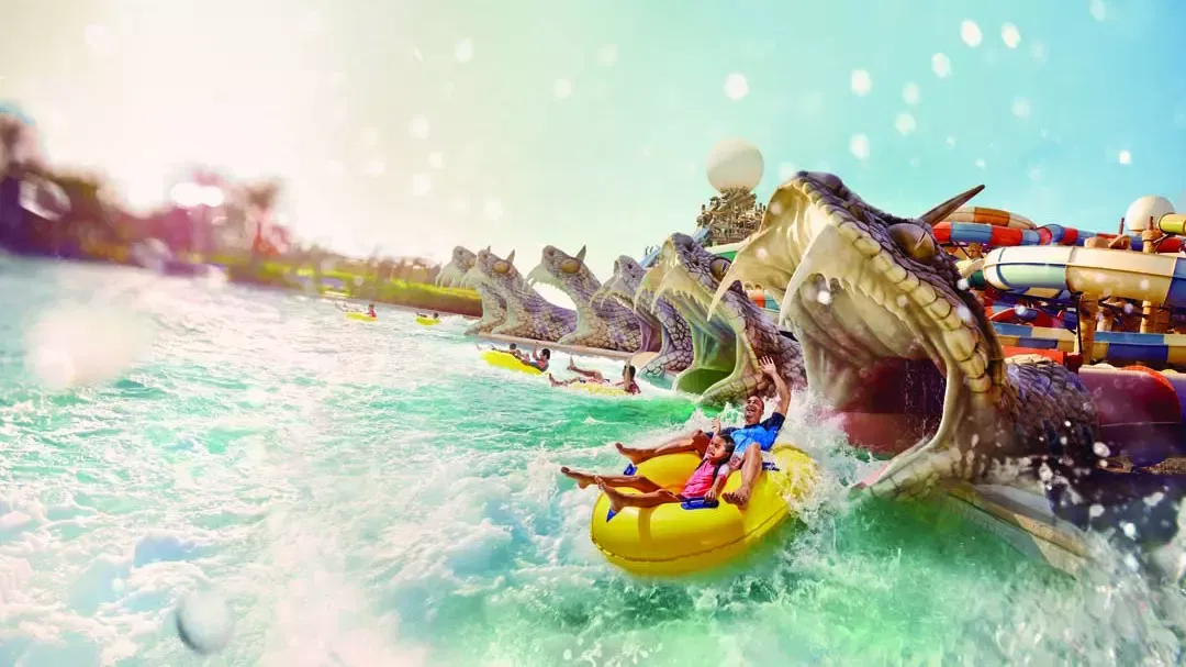 Two people on a yellow raft ride through churning water past a row of large sculpted dragon heads at Yas Waterworld, Abu Dhabi.
