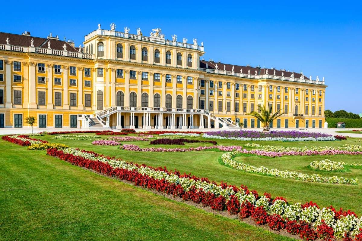 Front view of Schönbrunn Palace in Vienna, Austria, with colorful flowerbeds and a bright blue sky.