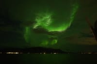Bright green Northern Lights stretching across the night sky above the sea