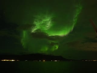 Bright green Northern Lights stretching across the night sky above the sea