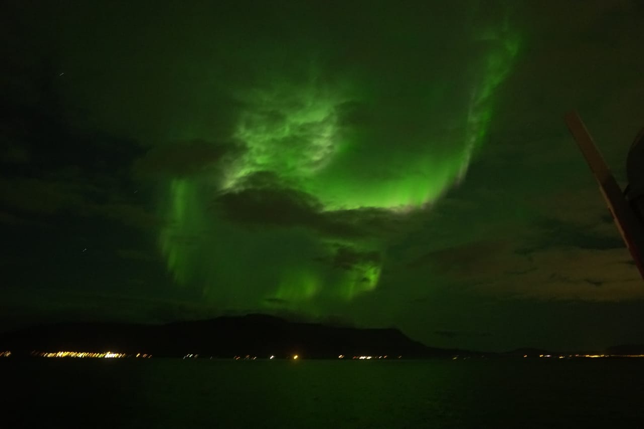 Bright green Northern Lights stretching across the night sky above the sea