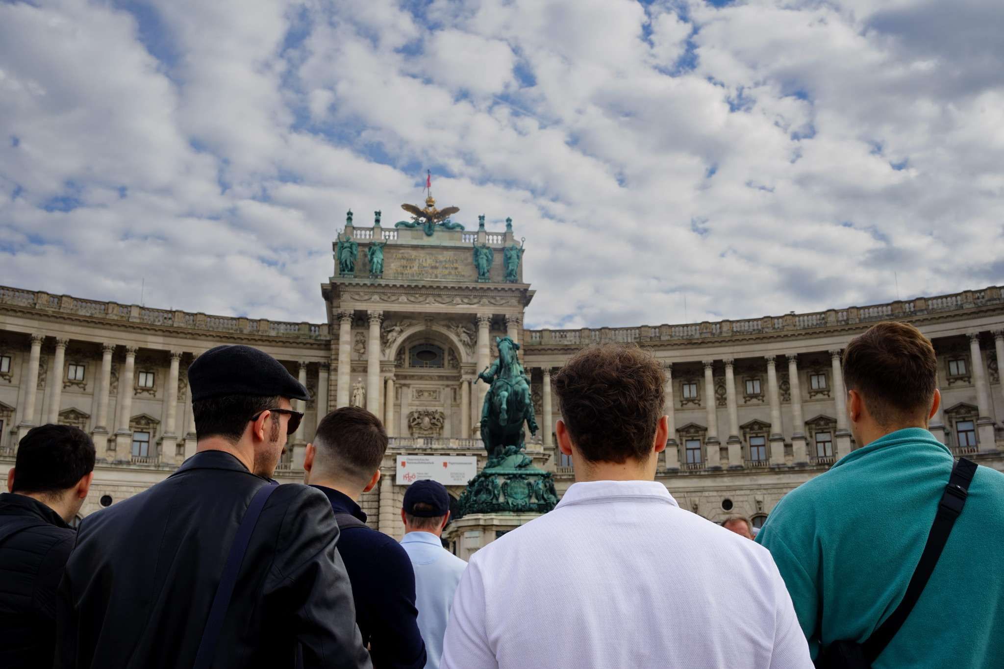 People facing the Hofburg Palace courtyard with a statue in the center under a cloudy sky