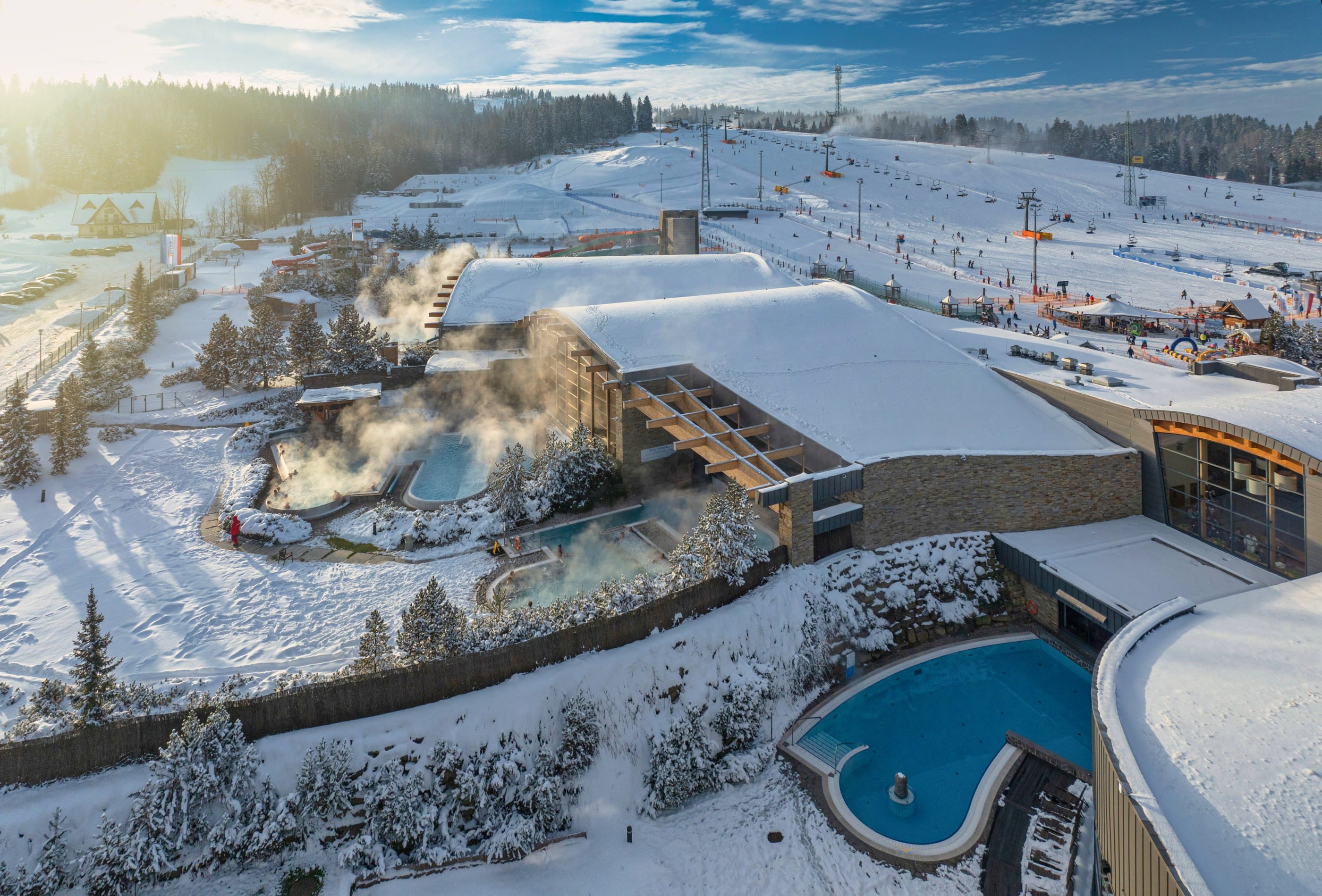 Aerial view of Terma Bania outdoor thermal pools in winter with steaming water and ski slopes in background