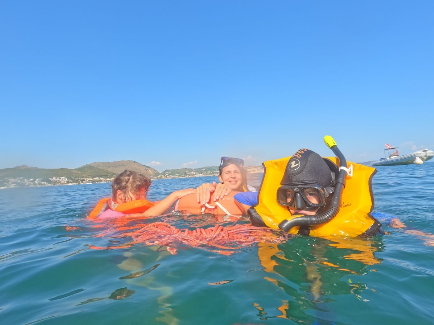 Three snorkelers in the sea surface having fun, with one of them wearing a life jacket as an additional safety measure