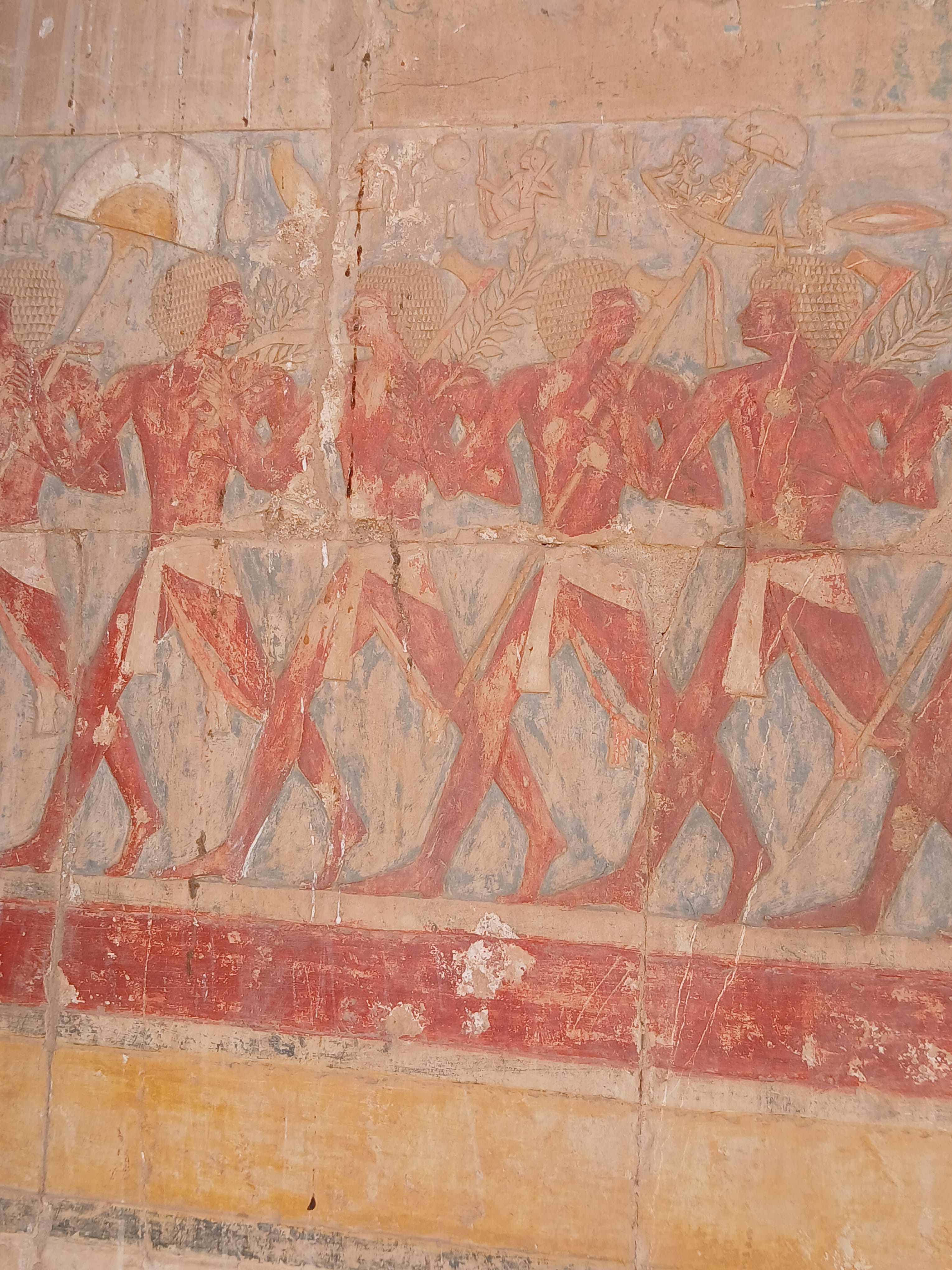 Row of ancient Egyptian soldiers painted in reddish-orange tones carved on a temple well