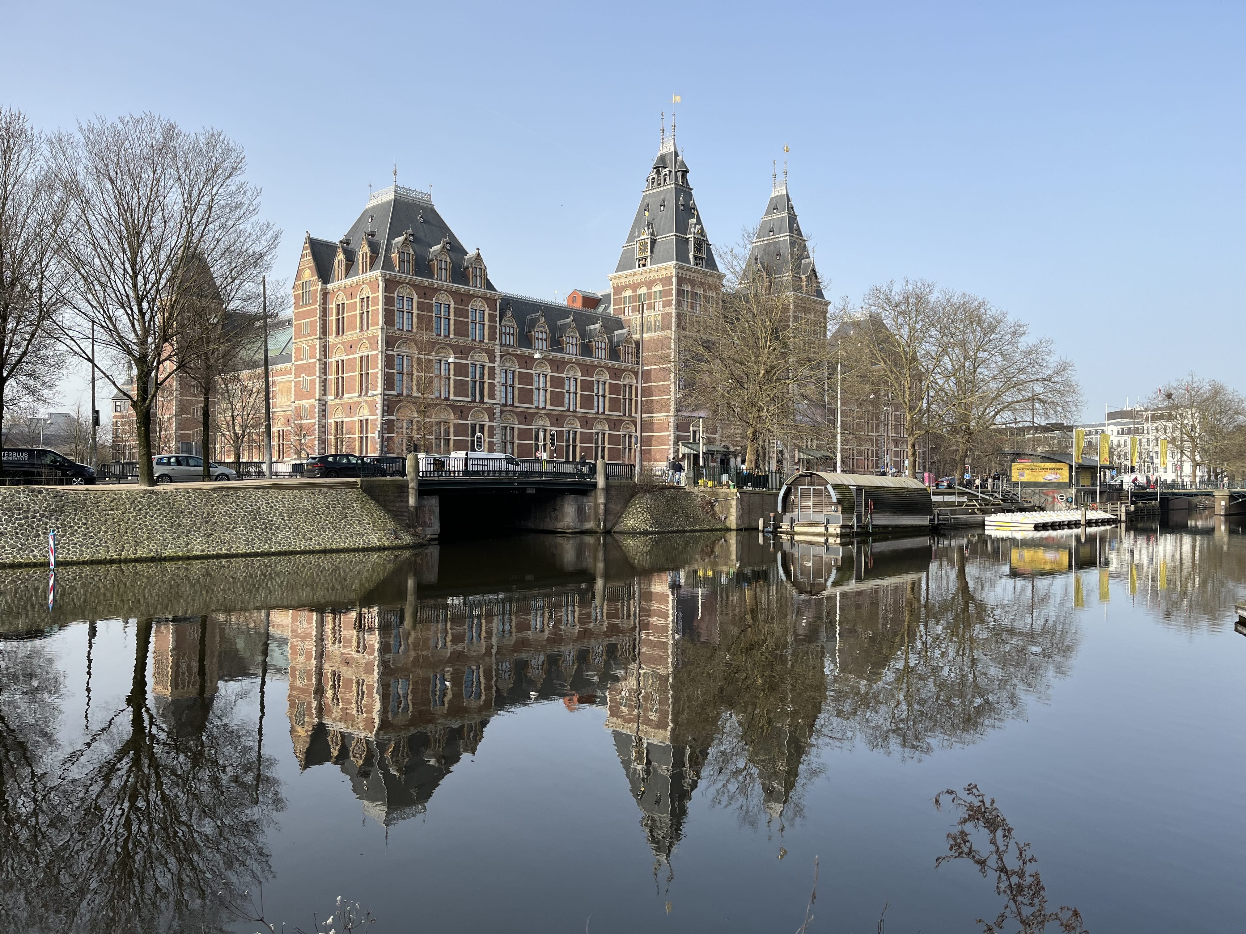 Rijksmuseum Amsterdam reflected in canal water with bridge and trees on a calm day
