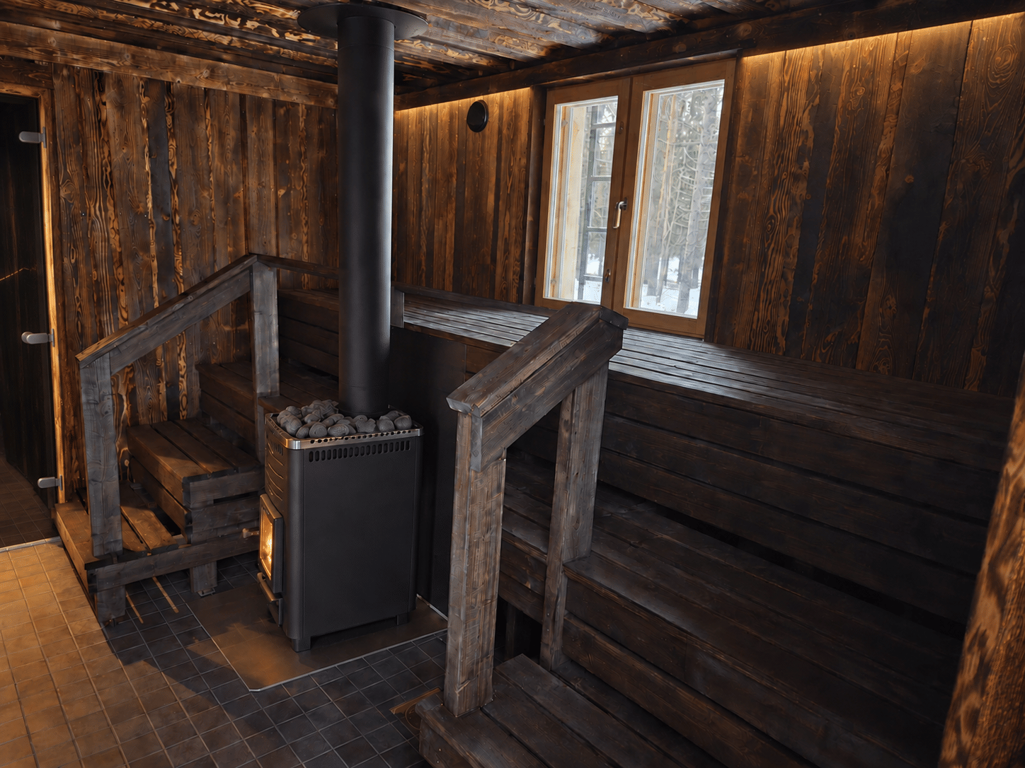 Traditional Finnish wood-fired sauna with dark timber benches, soft lighting and a central Harvia stove