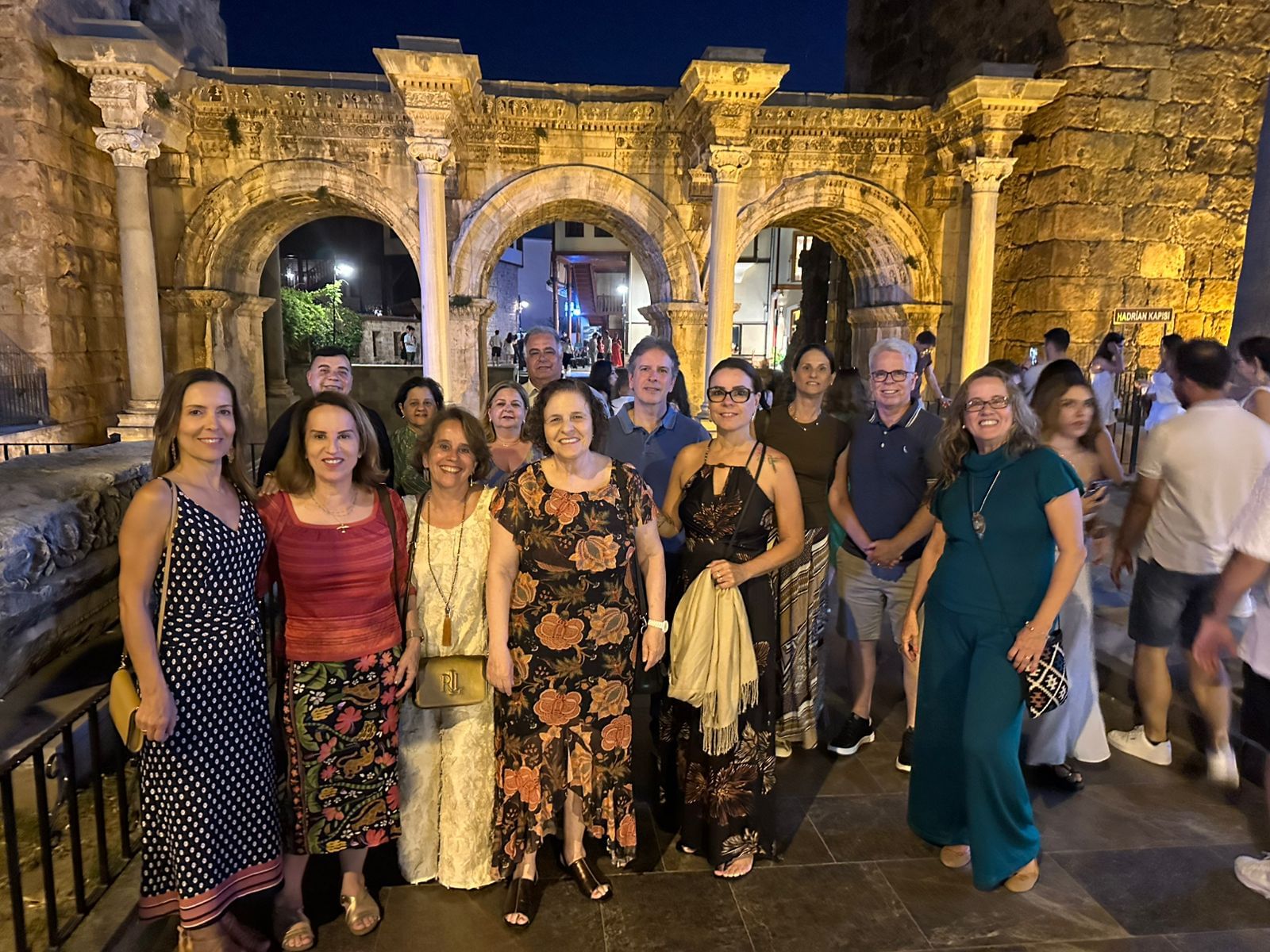 “A group of smiling travelers with their tour guides during an evening walk in Antalya, with softly lit streets and historic buildings in th