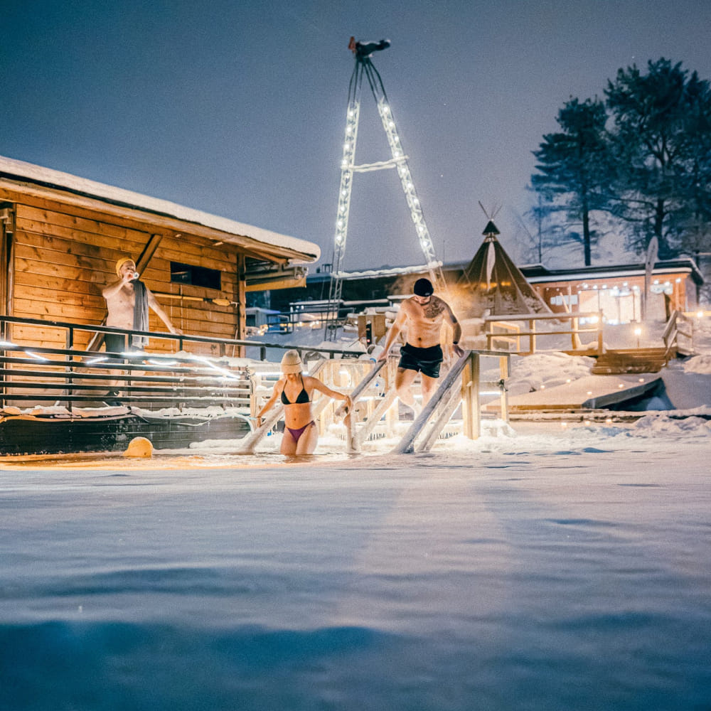 People going for a dip in the frozen river at Roiske Arctic Sauna Retreat