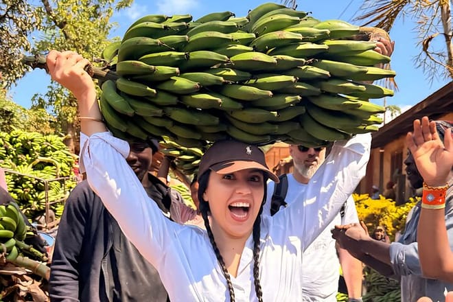 A happy tourist balancing a large bunch of bananas on her head in a Tanzanian village.