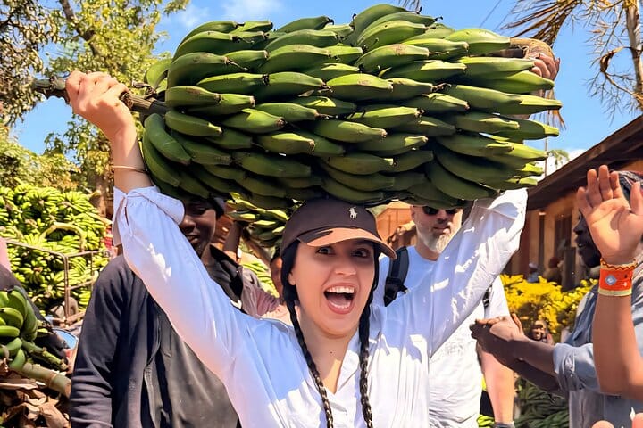 A happy tourist balancing a large bunch of bananas on her head in a Tanzanian village.