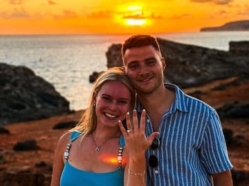 A joyful couple celebrating their engagement on a private boat in Malta, showing off the ring against the romantic glow of the sunset and the blue waters of Malta.