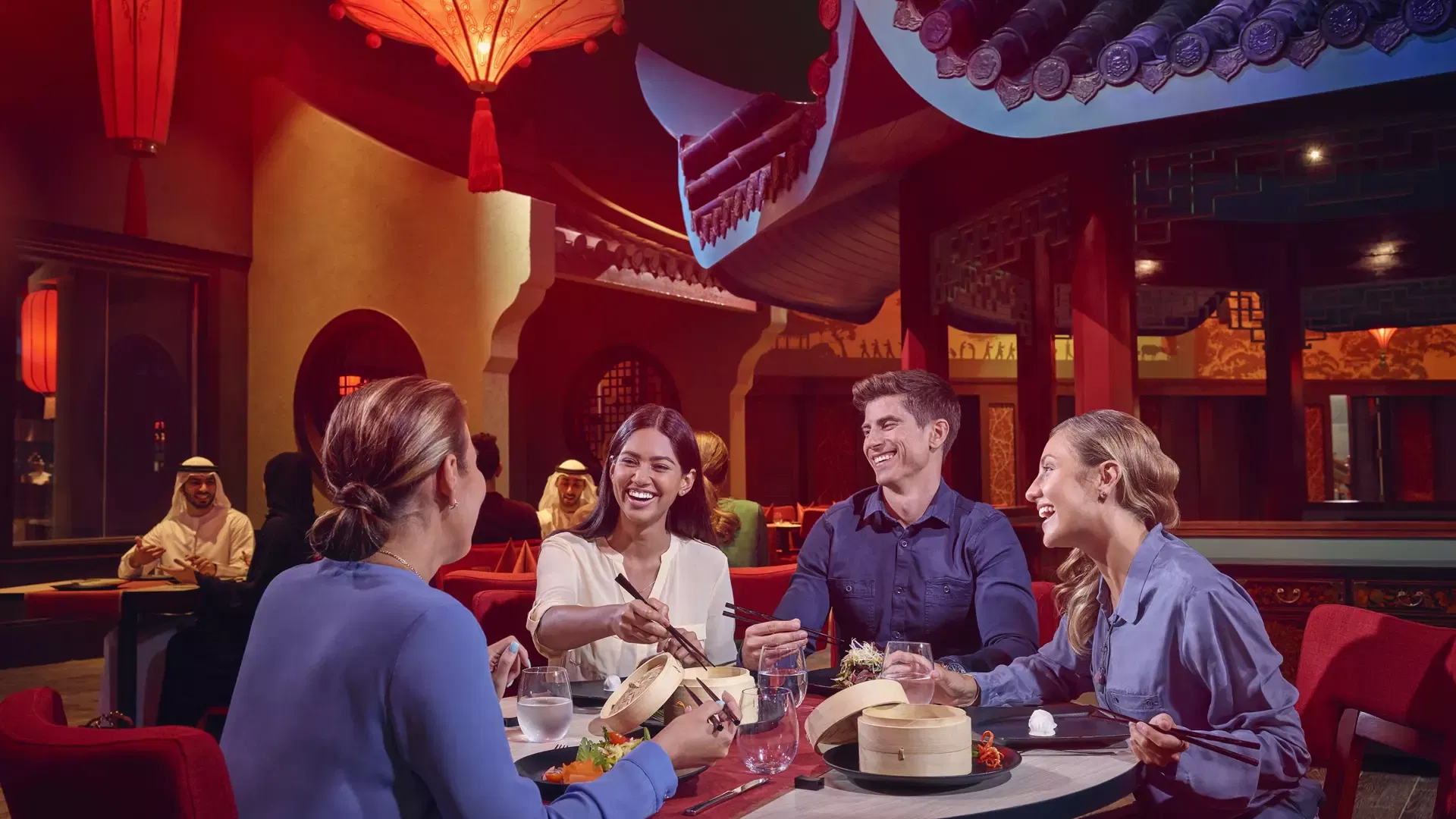 Four people sit around a table and laugh while eating Asian cuisine at IMG Worlds of Adventure Theme Park.